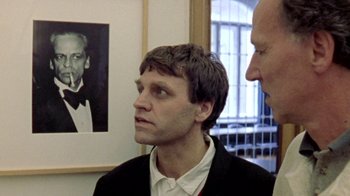 Movie still from “My Best Fiend” (1999), directed by Werner Herzog – Two men standing in front of a picture of a man; Close Up shot, Over the shoulder angle