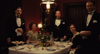 Movie still from “My Brilliant Career” (1979), directed by Gillian Armstrong – A group of people sitting around a table with a lamp; Medium shot, High angle