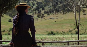 Movie still from “My Brilliant Career” (1979), directed by Gillian Armstrong – A woman standing on top of a wooden fence looking out at a field; Medium shot, Over the shoulder angle