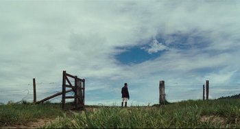Movie still from “My Brilliant Career” (1979), directed by Gillian Armstrong – A person standing in a grassy field near a fence; Extreme Wide shot, Low angle
