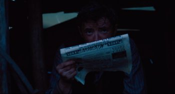 Movie still from “My Brilliant Career” (1979), directed by Gillian Armstrong – A man sitting down reading a newspaper at night; Close Up shot, Over the shoulder angle