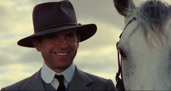 Movie still from “My Brilliant Career” (1979), directed by Gillian Armstrong – A man in a suit and hat standing next to a white horse; Close Up shot, Low angle
