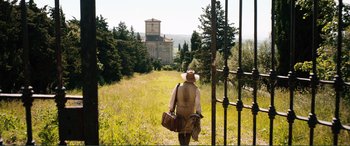 Movie still from “My Cousin Rachel” (2017), directed by Roger Michell – A person walking through a field with a bag and suitcase; Extreme Wide shot, Low angle