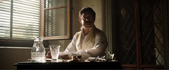 Movie still from “My Cousin Rachel” (2017), directed by Roger Michell – A man sitting at a table in front of a window; Medium shot, Low angle