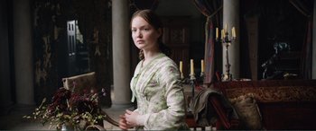 Movie still from “My Cousin Rachel” (2017), directed by Roger Michell – A young woman standing in front of a table; Medium shot, Over the shoulder angle