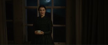 Movie still from “My Cousin Rachel” (2017), directed by Roger Michell – A woman holding a cup in front of a window at night; Medium shot, Low angle