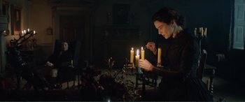 Movie still from “My Cousin Rachel” (2017), directed by Roger Michell – A woman lighting candles in a dark room; Medium shot, Over the shoulder angle
