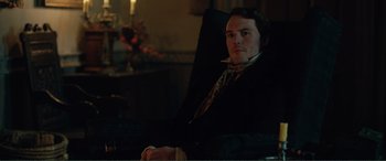 Movie still from “My Cousin Rachel” (2017), directed by Roger Michell – A man sitting in a chair in a dark room; Medium shot, Over the shoulder angle