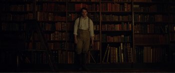 Movie still from “My Cousin Rachel” (2017), directed by Roger Michell – A man standing in front of a book shelf filled with lots of books; Wide shot, Low angle
