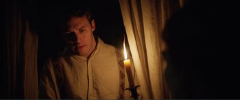 Movie still from “My Cousin Rachel” (2017), directed by Roger Michell – A man standing in front of a window holding a lit candle; Medium shot, Over the shoulder angle