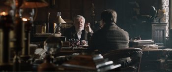 Movie still from “My Cousin Rachel” (2017), directed by Roger Michell – A man sitting at a table talking to another man; Medium shot, Over the shoulder angle