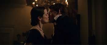 A man and a woman kissing each other in front of a chandelier