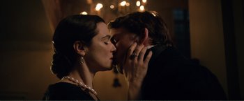 A man and a woman kissing each other in front of a chandelier