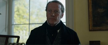 Movie still from “My Cousin Rachel” (2017), directed by Roger Michell – An older man wearing glasses and wearing a black coat; Close Up shot, Low angle