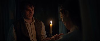 Movie still from “My Cousin Rachel” (2017), directed by Roger Michell – Two people sitting in front of a lit candle in a dark room; Medium shot, Over the shoulder angle
