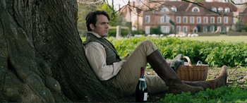 Movie still from “My Cousin Rachel” (2017), directed by Roger Michell – A man sitting on the ground next to a tree; Medium shot, Over the shoulder angle