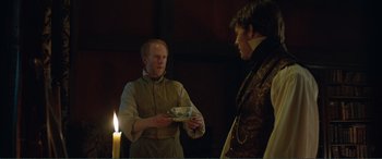 Movie still from “My Cousin Rachel” (2017), directed by Roger Michell – A man in a suit holding a plate in front of another man; Medium shot, Over the shoulder angle