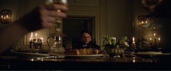 Movie still from “My Cousin Rachel” (2017), directed by Roger Michell – A man sitting at a table with a plate of food in front of him; Medium shot, Over the shoulder angle