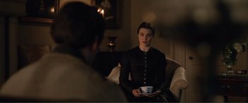 Movie still from “My Cousin Rachel” (2017), directed by Roger Michell – A woman sitting on top of a couch holding a coffee cup; Medium shot, Over the shoulder angle