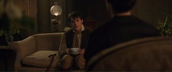 Movie still from “My Cousin Rachel” (2017), directed by Roger Michell – A man sitting on a couch holding a cup; Medium shot, Over the shoulder angle
