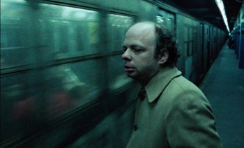 Movie still from “My Dinner with Andre” (1981), directed by Louis Malle – A man with a bald head standing in front of a train; Close Up shot, Low angle