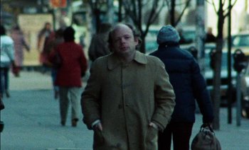 Movie still from “My Dinner with Andre” (1981), directed by Louis Malle – A man in a brown coat walking down a street; Medium shot, Low angle
