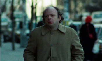 Movie still from “My Dinner with Andre” (1981), directed by Louis Malle – A man in a brown coat is walking down the street; Close Up shot, Over the shoulder angle
