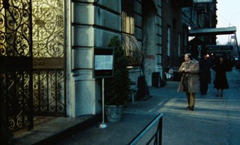 Movie still from “My Dinner with Andre” (1981), directed by Louis Malle – A woman standing on a sidewalk next to a building; Wide shot, Over the shoulder angle