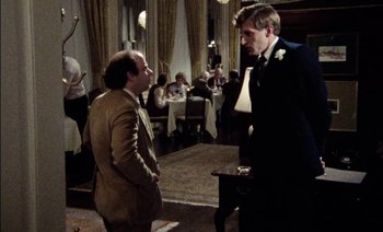 Movie still from “My Dinner with Andre” (1981), directed by Louis Malle – Two men in suits talking to each other in front of a table; Wide shot, Over the shoulder angle