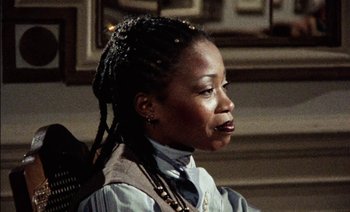 Movie still from “My Dinner with Andre” (1981), directed by Louis Malle – A woman with a long dreadlocks wearing a shirt and tie; Close Up shot, Low angle