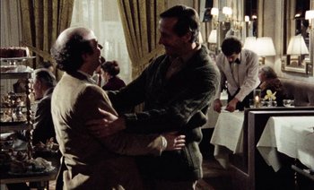 Movie still from “My Dinner with Andre” (1981), directed by Louis Malle – Two men hugging each other in front of other people; Medium shot, Over the shoulder angle