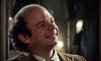 Movie still from “My Dinner with Andre” (1981), directed by Louis Malle – A man with a bald head smiling for the camera; Close Up shot, Over the shoulder angle