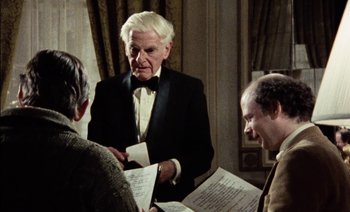 Movie still from “My Dinner with Andre” (1981), directed by Louis Malle – A man in a tuxedo is holding a sheet of paper; Medium shot, Over the shoulder angle