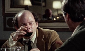 Movie still from “My Dinner with Andre” (1981), directed by Louis Malle – A man drinking a glass of wine at a table; Close Up shot, Over the shoulder angle