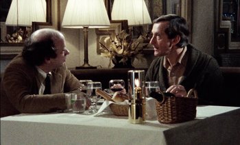 Movie still from “My Dinner with Andre” (1981), directed by Louis Malle – Two men are sitting at a table talking to each other; Medium shot, Over the shoulder angle