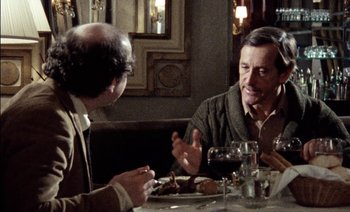 Movie still from “My Dinner with Andre” (1981), directed by Louis Malle – Two men sitting at a table in front of a plate of food; Medium shot, Over the shoulder angle