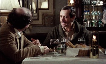 Movie still from “My Dinner with Andre” (1981), directed by Louis Malle – Two men sitting at a table with a glass of red wine; Medium shot, Over the shoulder angle