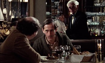 Movie still from “My Dinner with Andre” (1981), directed by Louis Malle – A man sitting at a table with a glass of wine; Medium shot, Over the shoulder angle