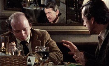 Movie still from “My Dinner with Andre” (1981), directed by Louis Malle – A group of people sitting at a table with a glass of wine; Medium shot, Over the shoulder angle