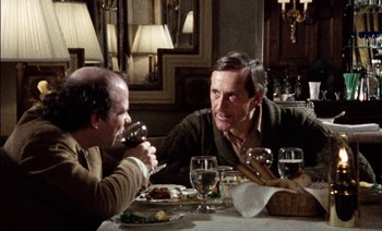 Movie still from “My Dinner with Andre” (1981), directed by Louis Malle – Two men sitting at a dinner table drinking red wine; Medium shot, Over the shoulder angle
