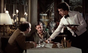 Movie still from “My Dinner with Andre” (1981), directed by Louis Malle – Three men sitting at a table in front of a waiter; Medium shot, Over the shoulder angle