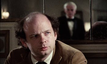 Movie still from “My Dinner with Andre” (1981), directed by Louis Malle – A man with a bald head sitting in front of another man; Close Up shot, Over the shoulder angle