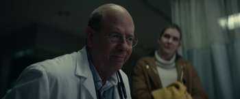 Movie still from “Fractured” (2019), directed by Brad Anderson – An older man wearing glasses and a lab coat; Close Up shot, Over the shoulder angle