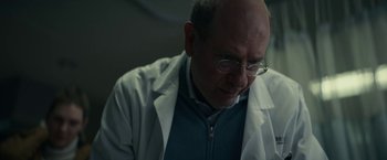 Movie still from “Fractured” (2019), directed by Brad Anderson – An older man wearing glasses and a lab coat; Close Up shot, Low angle