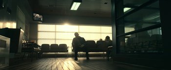 Movie still from “Fractured” (2019), directed by Brad Anderson – Two people sitting in a waiting room in the sunlight; Wide shot, Low angle