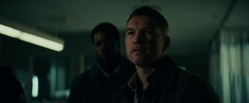 Movie still from “Fractured” (2019), directed by Brad Anderson – A man standing next to another man in a dark room; Close Up shot, Low angle