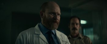 Movie still from “Fractured” (2019), directed by Brad Anderson – A man in a lab coat and a tie; Close Up shot, Over the shoulder angle