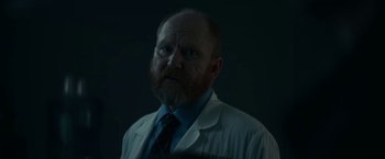 Movie still from “Fractured” (2019), directed by Brad Anderson – A man in a lab coat and a tie; Close Up shot, Low angle