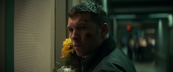 Movie still from “Fractured” (2019), directed by Brad Anderson – A person wearing a jacket near flowers; Close Up shot, Over the shoulder angle