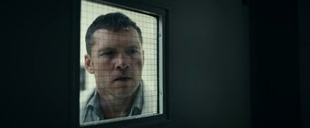 Movie still from “Fractured” (2019), directed by Brad Anderson – A man looking out a window through a wire fence; Close Up shot, Over the shoulder angle